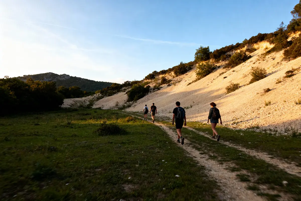 Groupe de randonneurs marchant sur un sentier au coucher du soleil, entouré de collines désertiques et végétation clairsemée.
