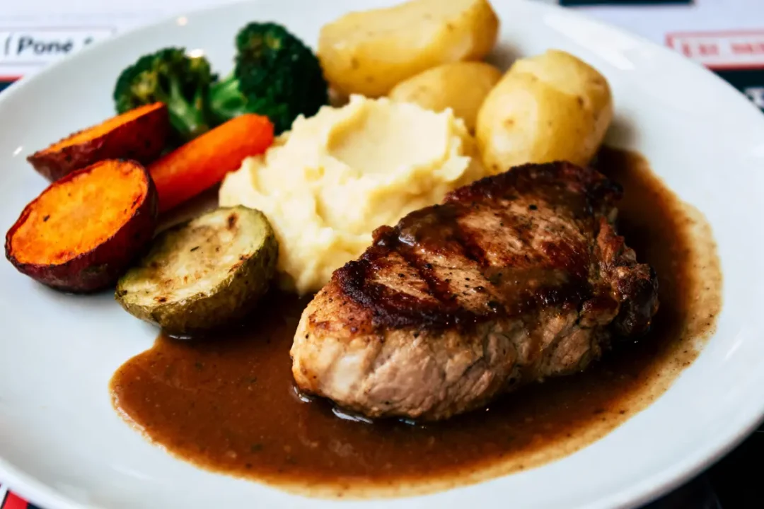 Assiette avec viande grillée, purée, légumes variés et pommes de terre, nappée de sauce brune.