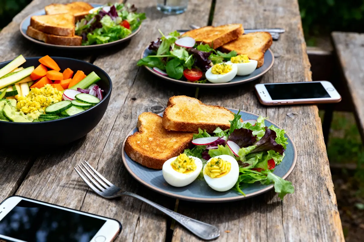 Assiettes de salade, toasts, œufs, avec des téléphones sur une table en bois, en plein air.