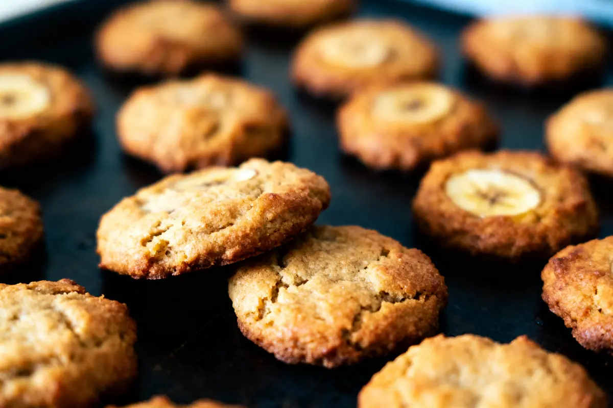 Biscuits dorés avec tranches de banane sur plaque de cuisson noire, en gros plan.