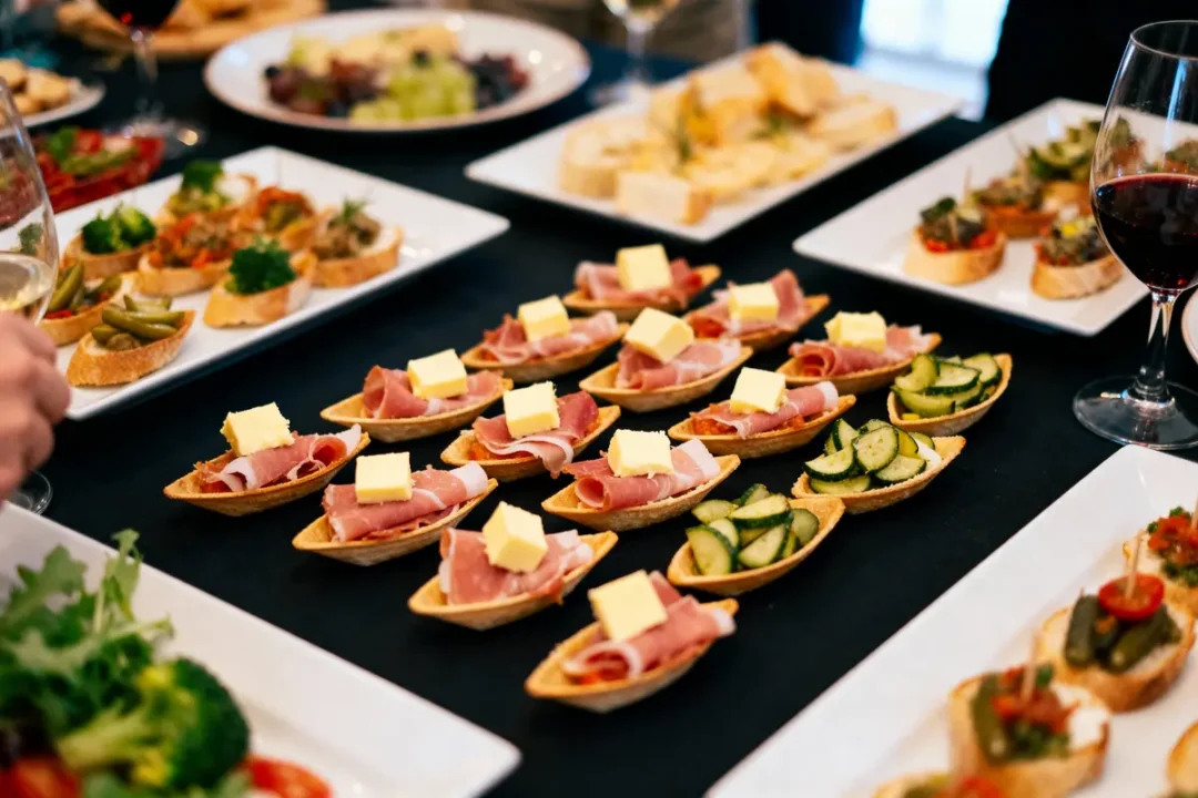 Assortiment de canapés avec charcuterie, concombres, fromage, sur table, accompagnés de verres de vin rouge.