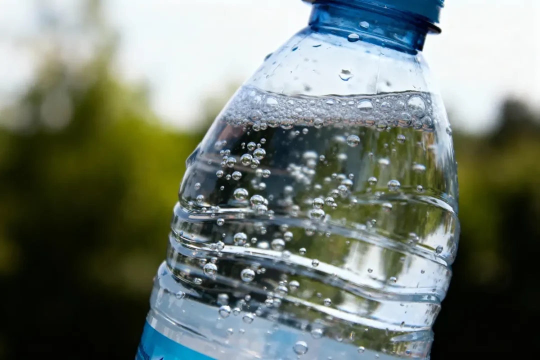 Bouteille d'eau plastique transparente avec des bulles, fond flou et verdoyant.