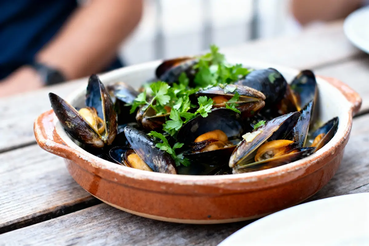 Assiette de moules garnies de persil dans un plat en terre cuite sur une table en bois.