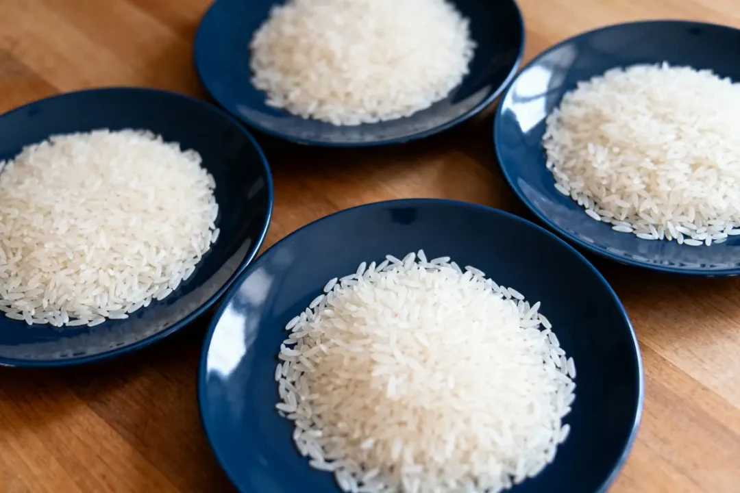 Quatre assiettes bleues contenant du riz blanc, disposées sur une table en bois.