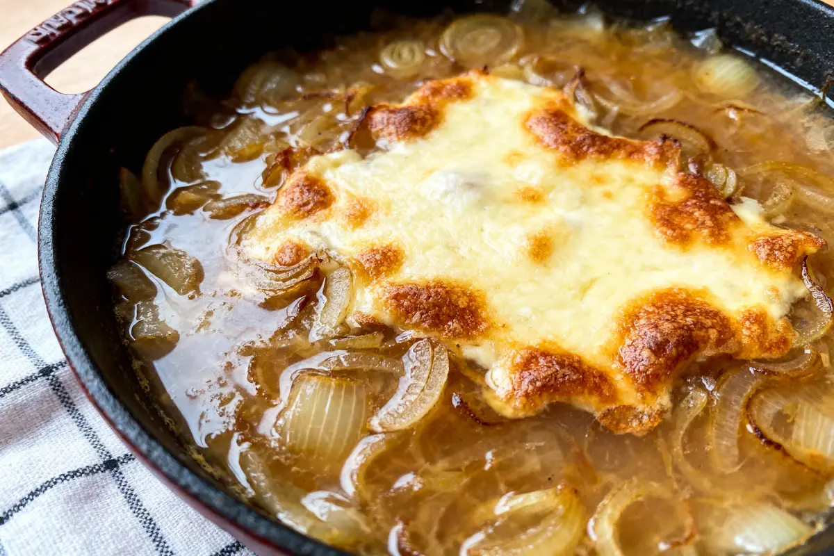 Gratin de soupe à l'oignon dans une cocotte noire sur nappe à carreaux blancs et noirs.