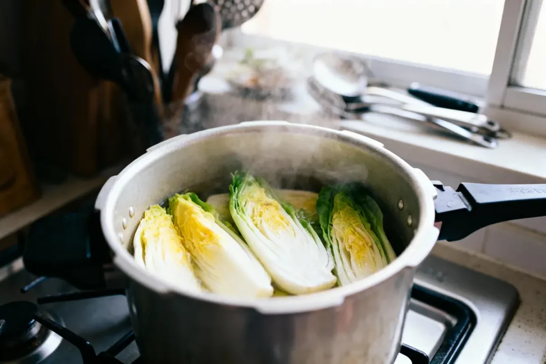 Quarts de chou chinois cuisant à la vapeur dans une casserole sur la cuisinière d'une cuisine ensoleillée.