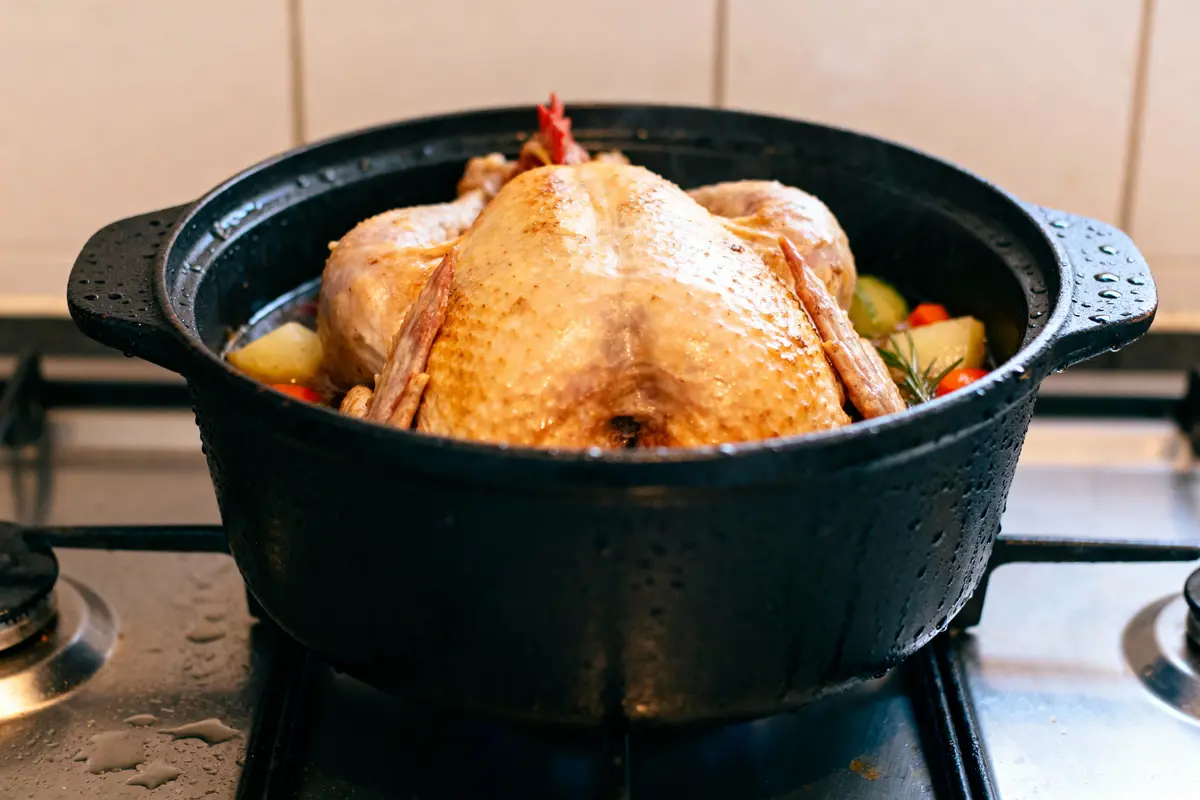 Poulet entier rôti dans une cocotte noire, avec légumes, sur une cuisinière.