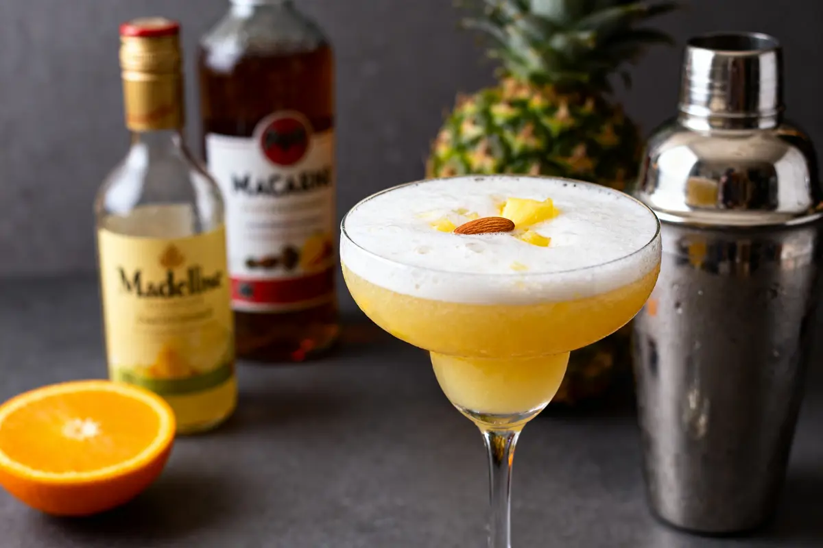 Verre de cocktail Madeleine avec ananas, orange et bouteille sur table grise