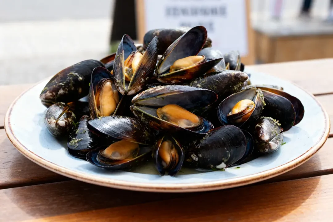 Assiette de moules fraîches sur table en bois explorant combien de moules par personne.