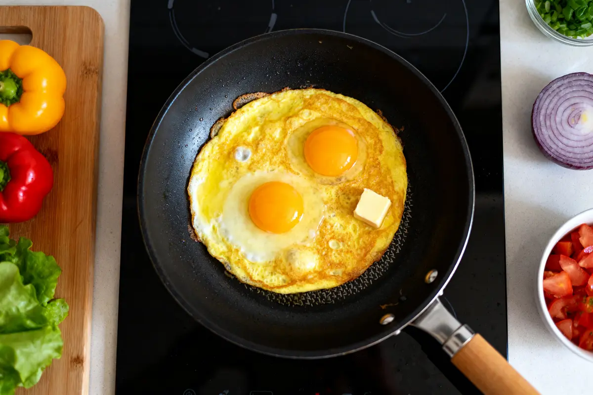 Deux œufs et beurre dans poêle, recette d'omelette avec légumes autour